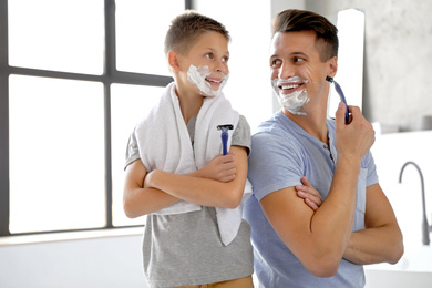 Photo of Happy father and son with shaving foam on their faces in bathroom