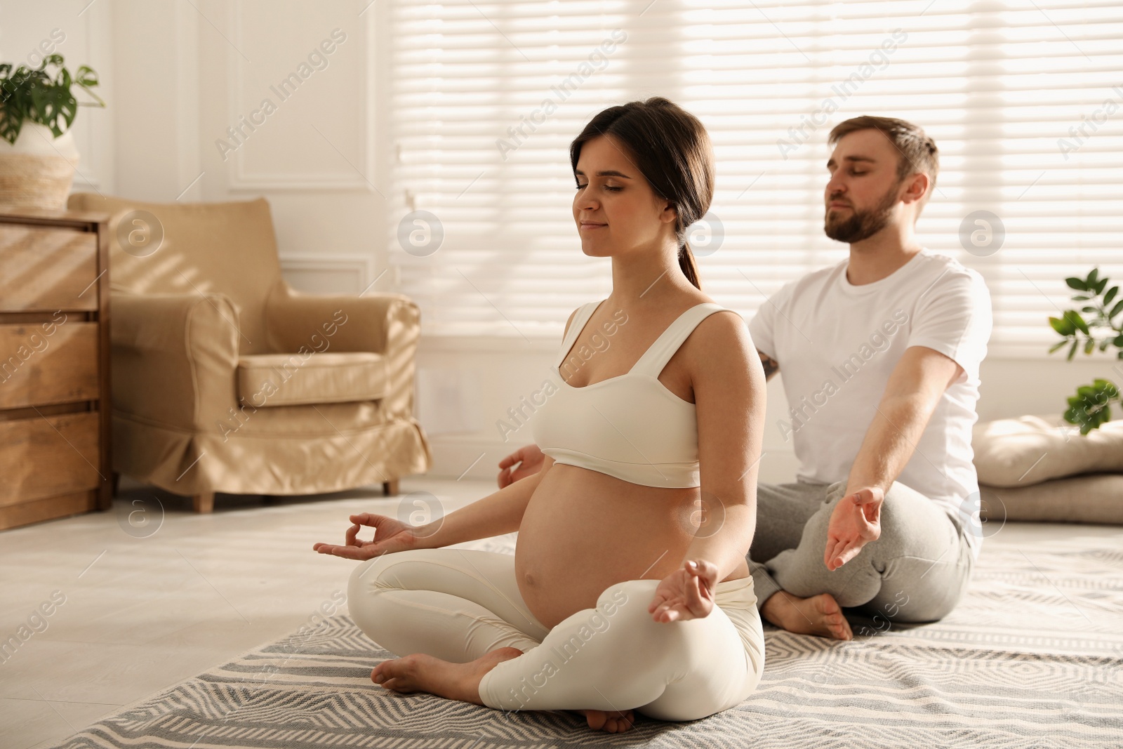 Photo of Young pregnant woman with her husband practicing yoga at home