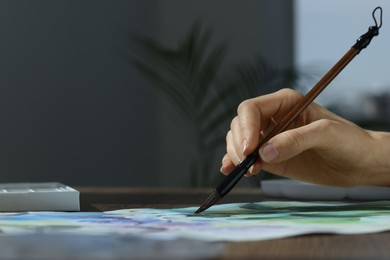 Photo of Woman painting flowers with watercolor at wooden table, closeup. Space for text