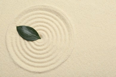 Zen rock garden. Circle pattern and green leaf on beige sand, top view