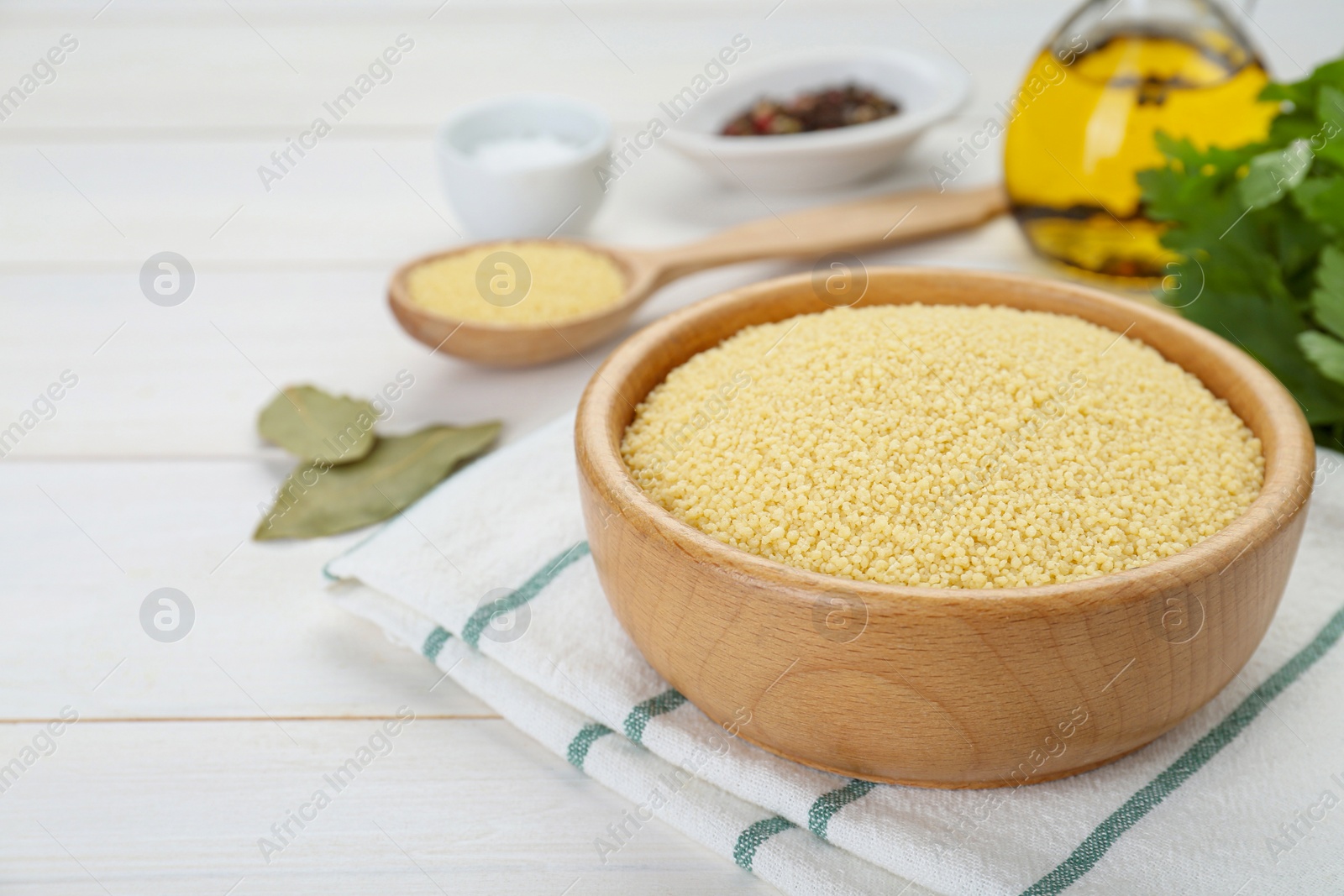 Photo of Bowl of raw couscous on white wooden table, closeup. Space for text