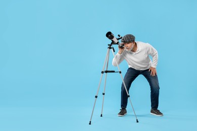 Senior astronomer looking at stars through telescope on light blue background Space for text