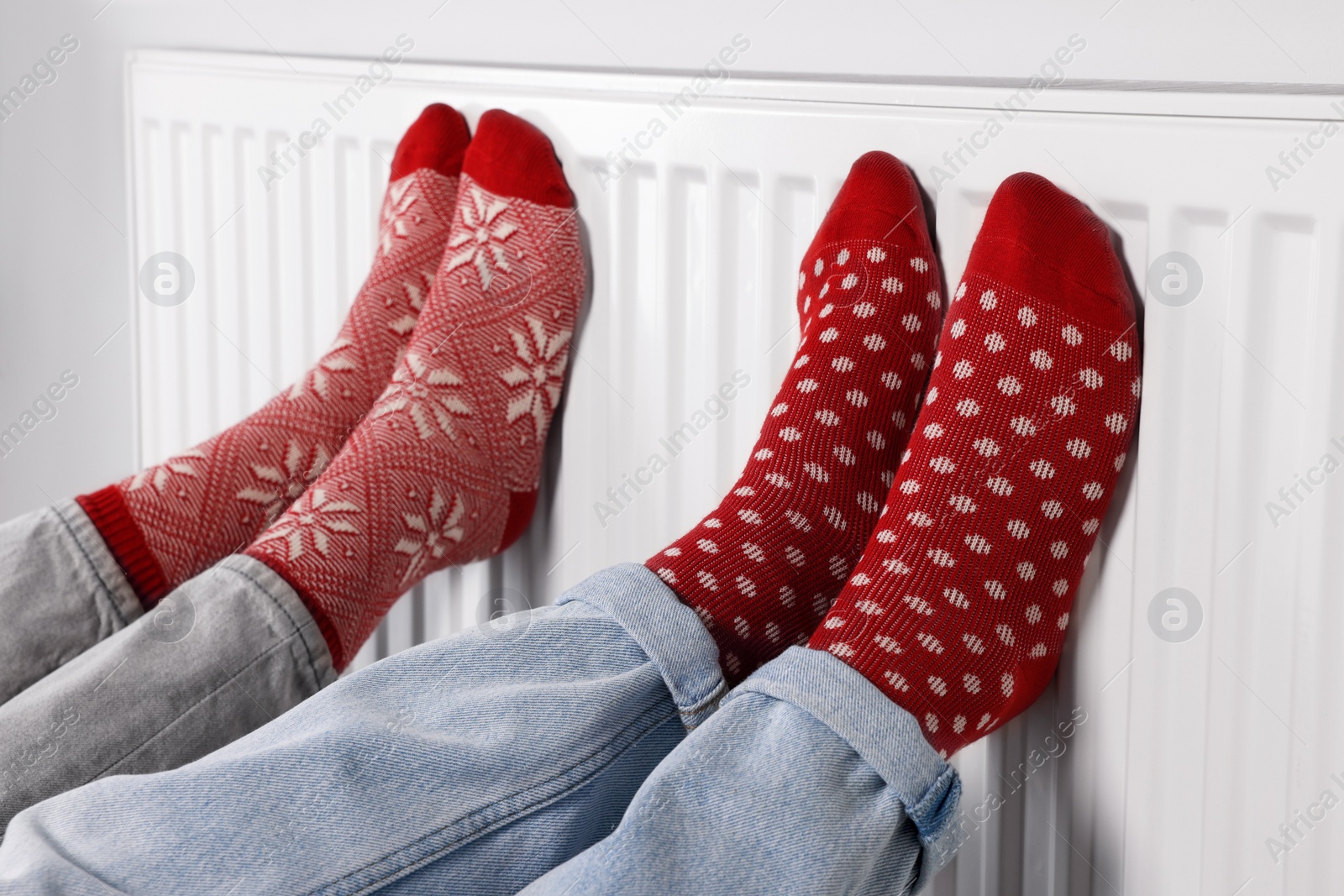 Photo of People warming feet near heating radiator indoors, closeup