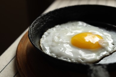 Photo of Frying pan with tasty cooked egg on wooden board, closeup