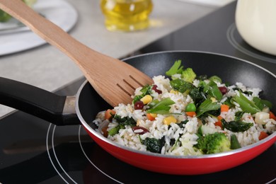 Frying tasty rice with vegetables on induction stove in kitchen, closeup