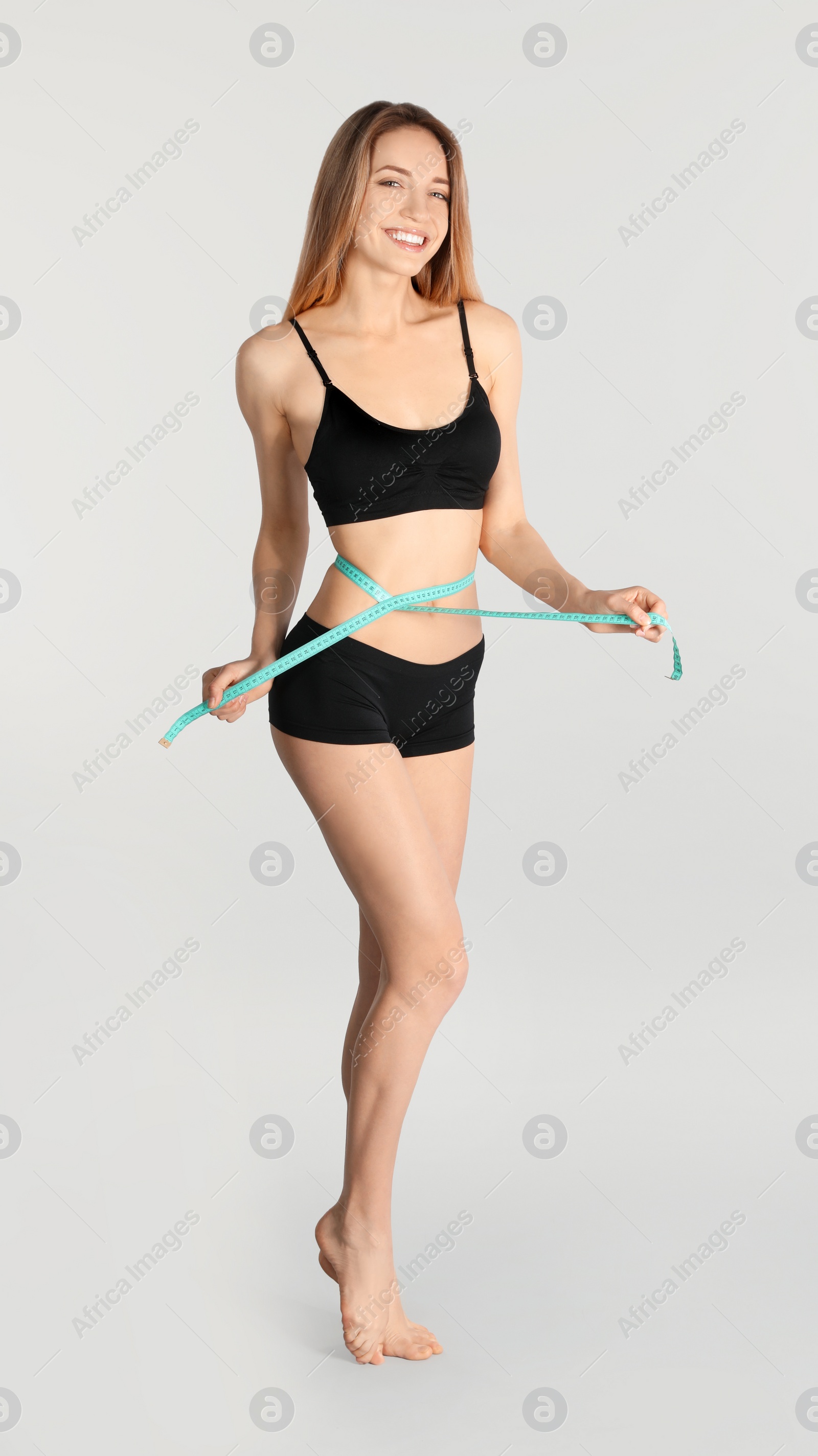 Photo of Slim woman measuring her waist on light background. Perfect body