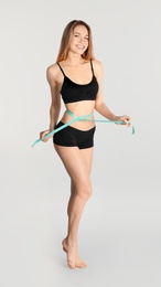 Photo of Slim woman measuring her waist on light background. Perfect body