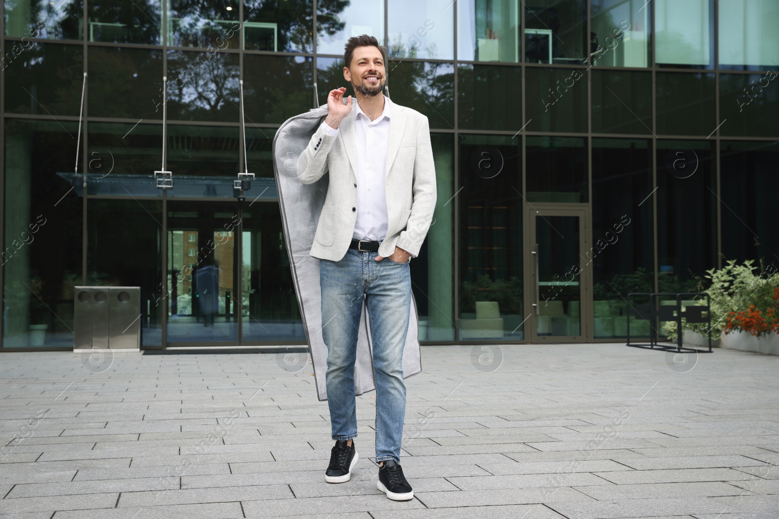 Photo of Attractive happy man holding garment cover with clothes outdoors. Dry cleaning service