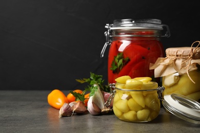 Glass jars with pickled peppers on grey table. Space for text