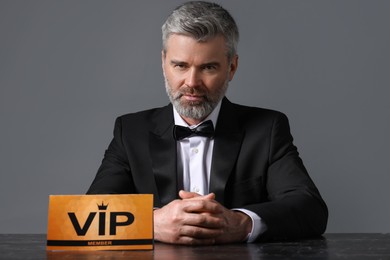 Handsome man sitting at table with VIP sign on grey background