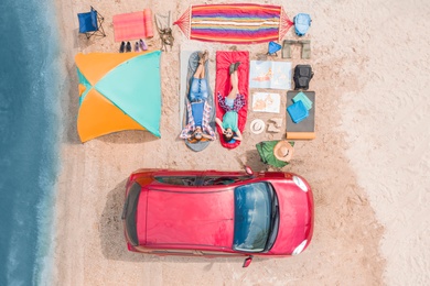 Couple with camping equipment near car on sand, aerial view. Summer trip