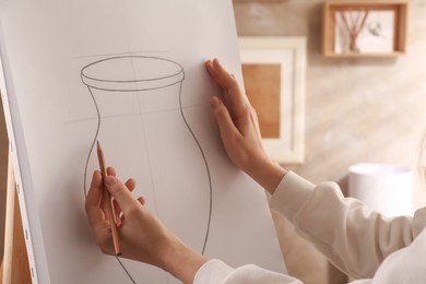 Photo of Woman drawing vase with graphite pencil on canvas indoors, closeup