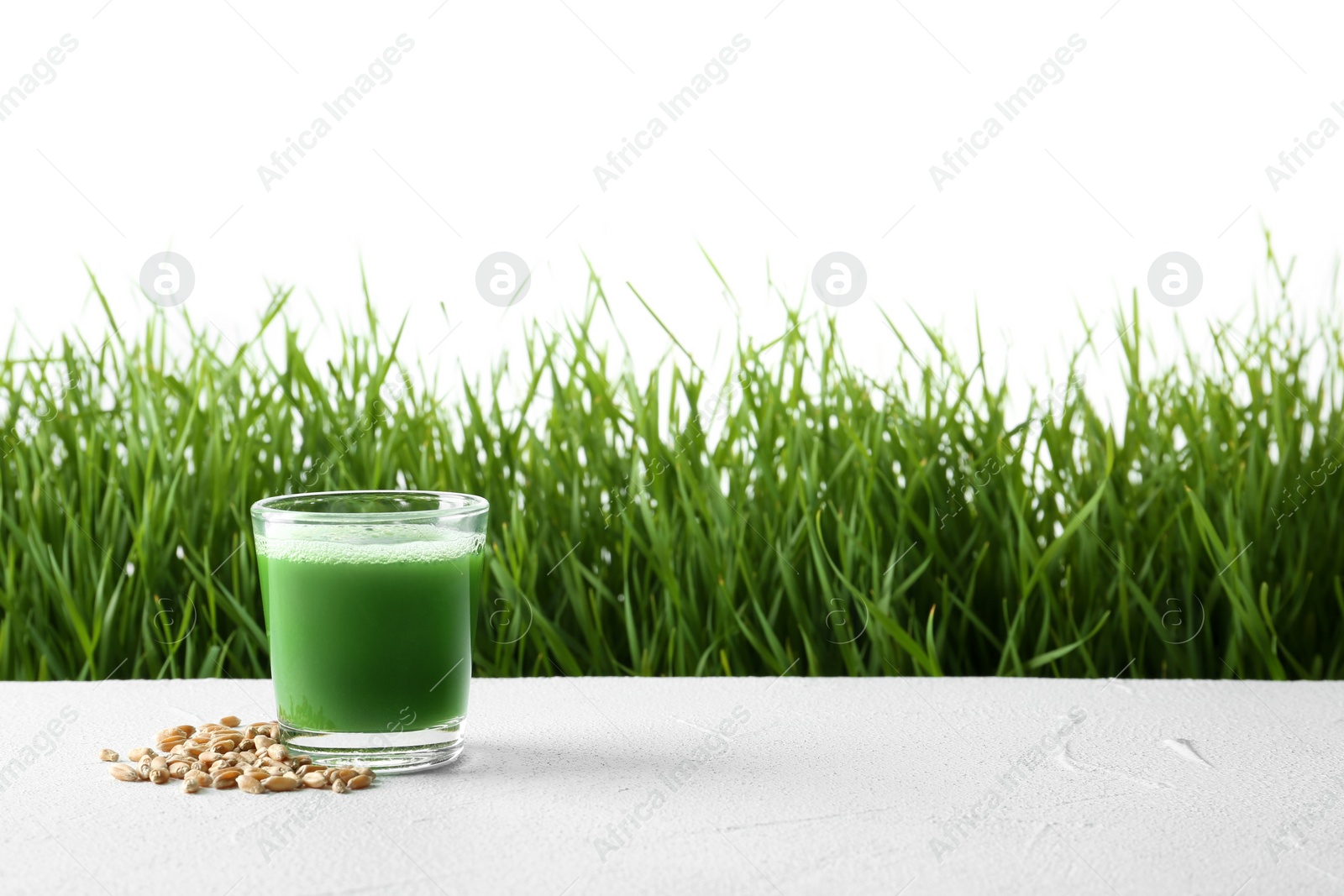 Glass of juice with grains on table and fresh wheat grass against white background. Space for text Photo of Glass of juice with grains on table and fresh wheat grass against white background. Space for text