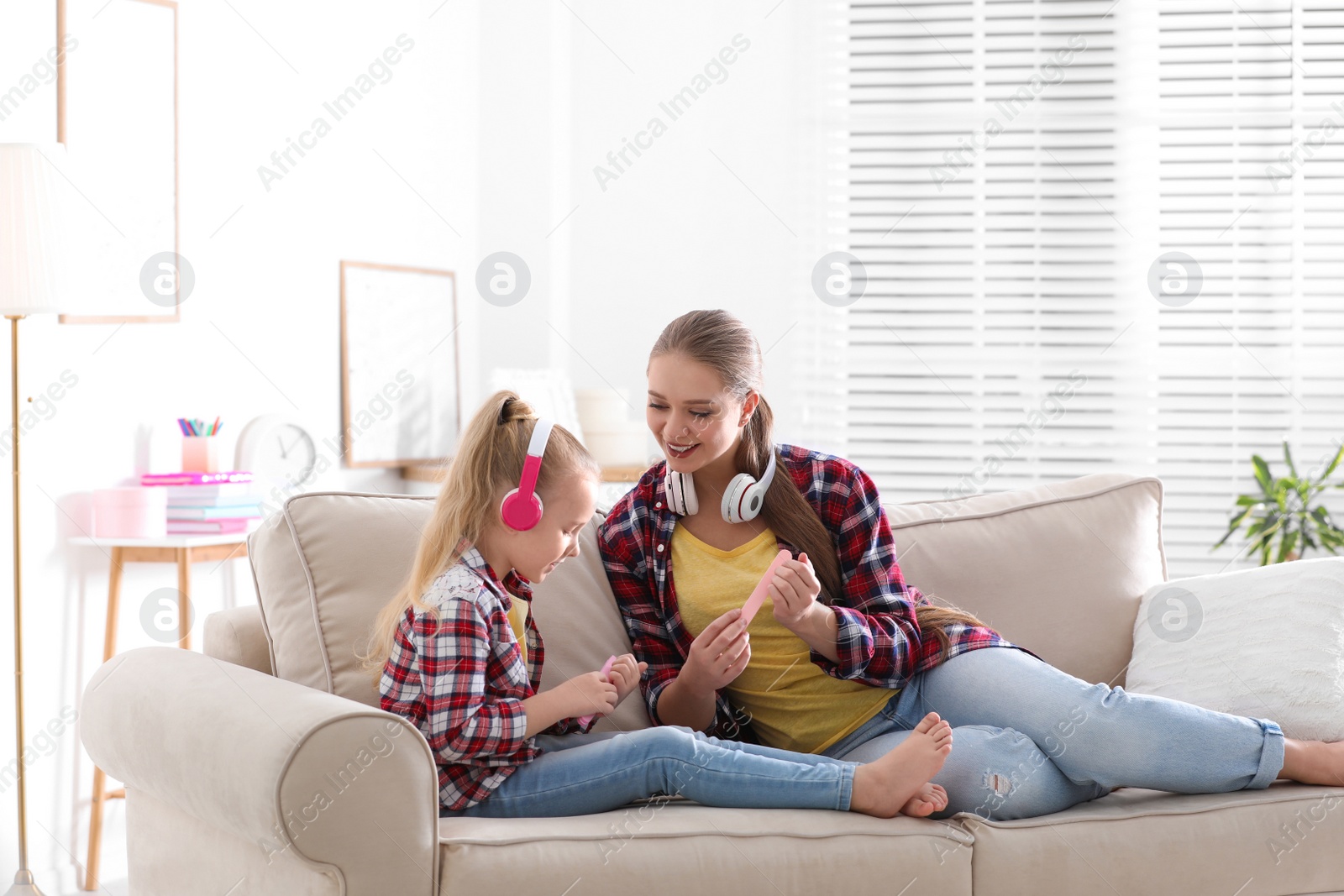 Photo of Happy mother and little daughter with headphones filing nails on sofa at home