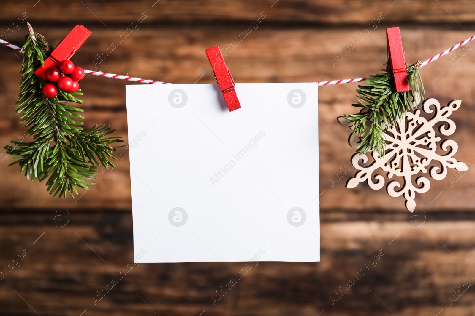 Photo of Blank Christmas card and festive decor on rope against wooden background. Space for text