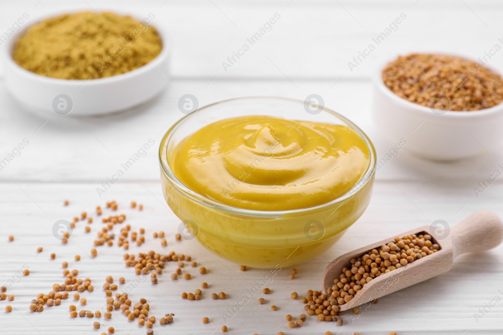 Photo of Bowl with delicious mustard and seeds on white wooden table