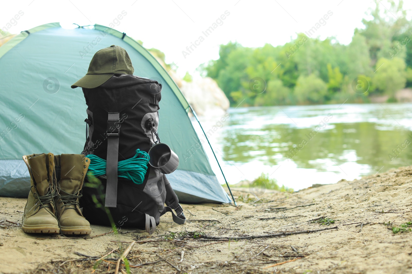 Photo of Modern camping tent and equipment on riverbank. Space for text