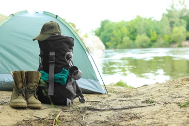 Modern camping tent and equipment on riverbank. Space for text