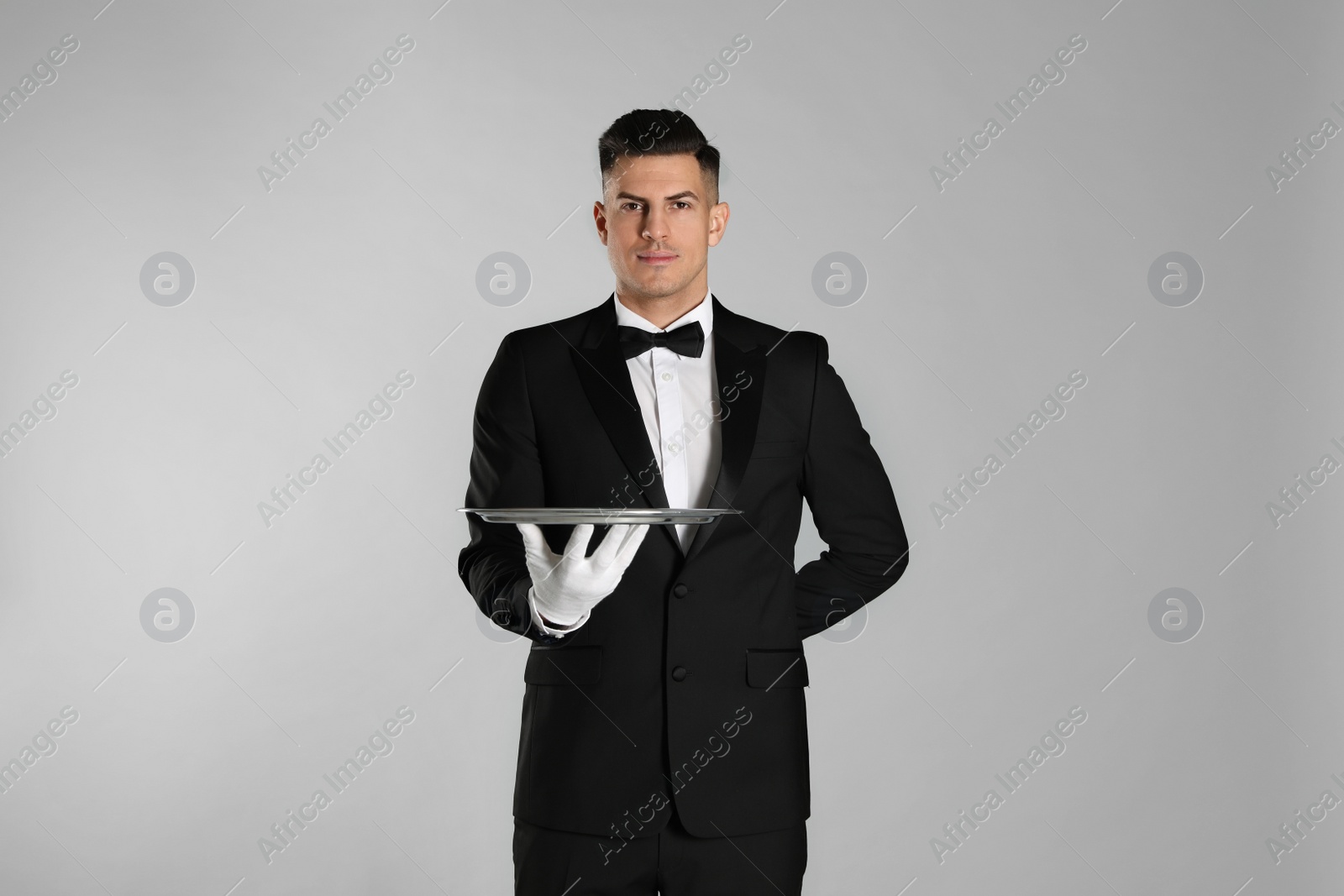 Photo of Handsome butler with tray on light grey background