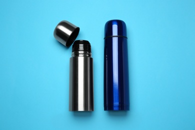 Photo of Stainless steel thermoses on light blue background, flat lay