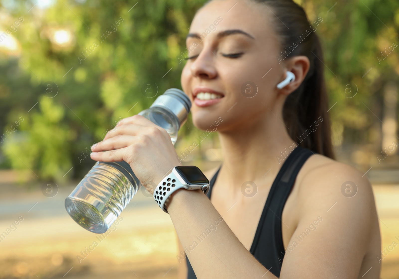 Photo of Woman with modern smart watch drinking water outdoors