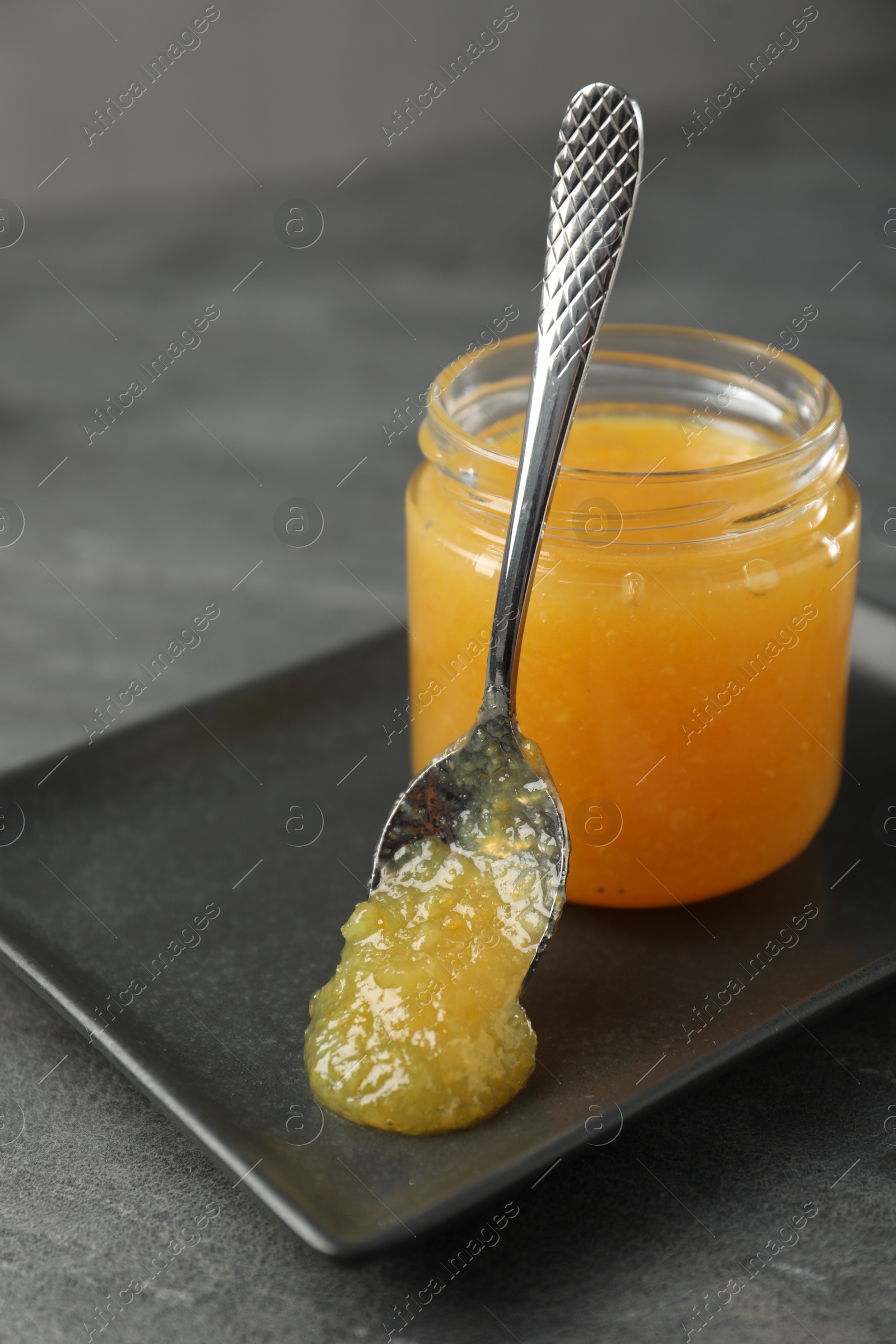 Photo of Delicious orange marmalade in jar and spoon on grey table