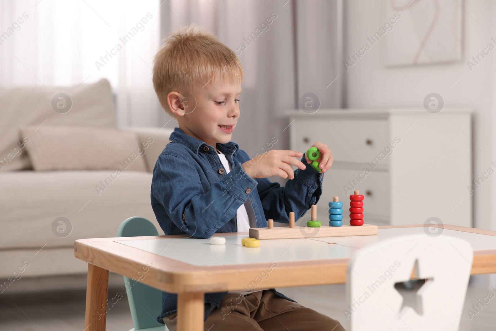 Photo of Cute little boy playing with stacking and counting game at table indoors. Child's toy