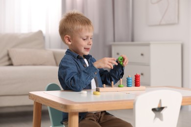 Photo of Cute little boy playing with stacking and counting game at table indoors. Child's toy
