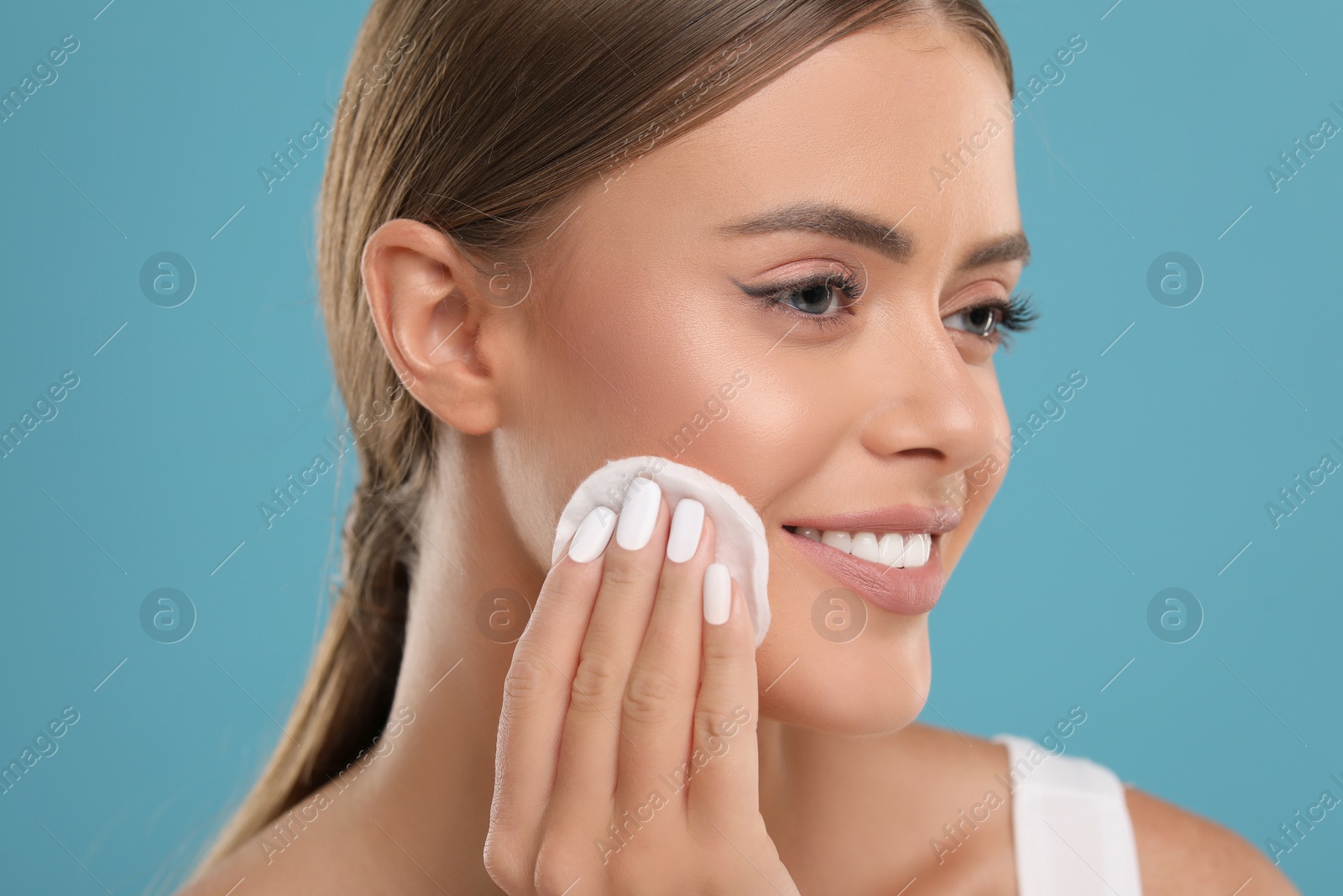 Photo of Beautiful woman removing makeup with cotton pad on light blue background, closeup