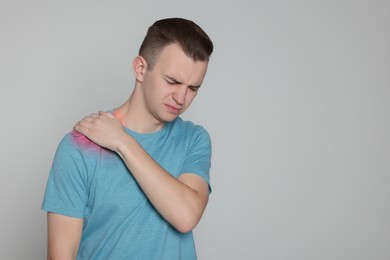 Man suffering from pain in shoulder on grey background. Space for text