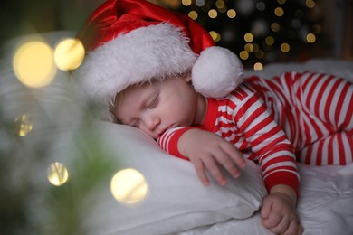 Photo of Baby in Christmas pajamas and Santa hat sleeping on bed indoors