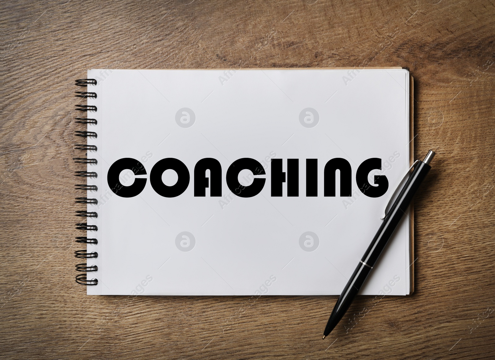 Image of Adult learning. Notebook with word COACHING and pen on wooden table, top view