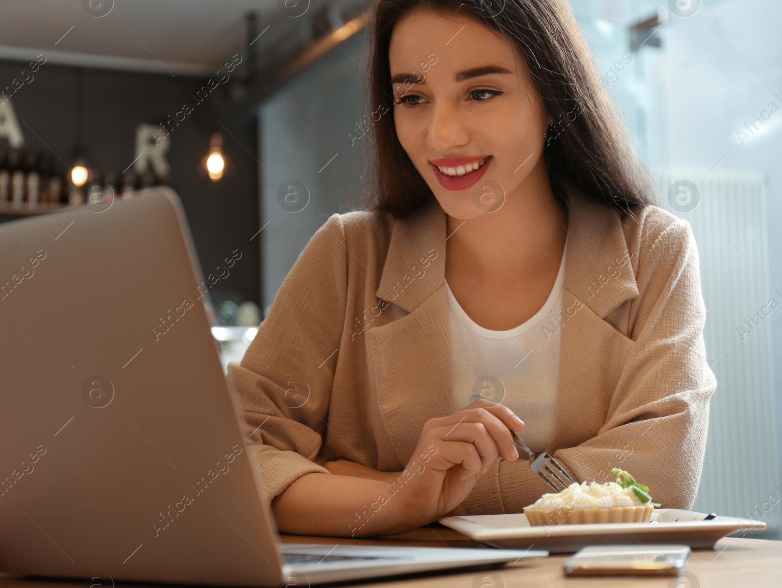 Photo of Young blogger with laptop eating cake in cafe