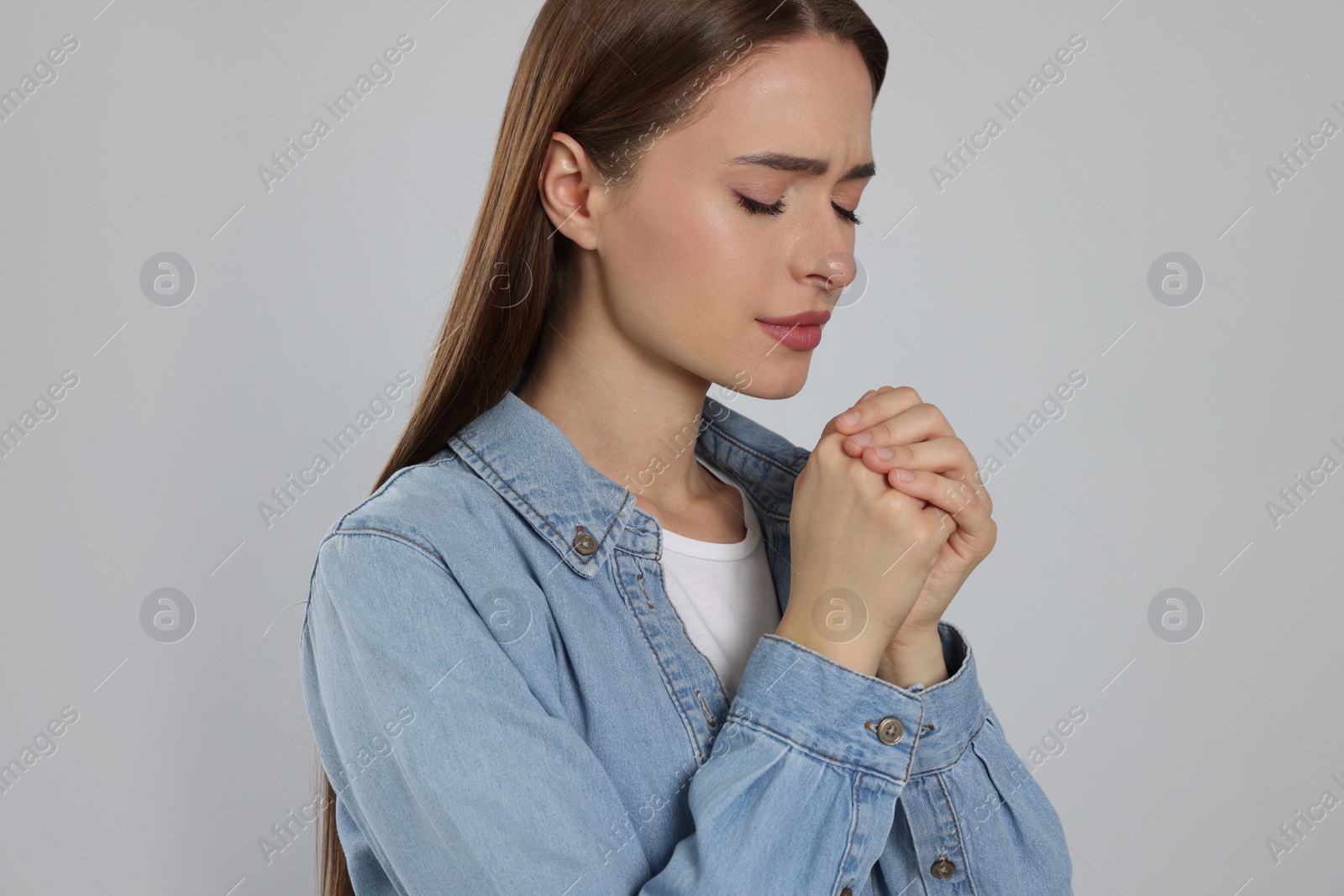 Photo of Woman with clasped hands praying on light grey background