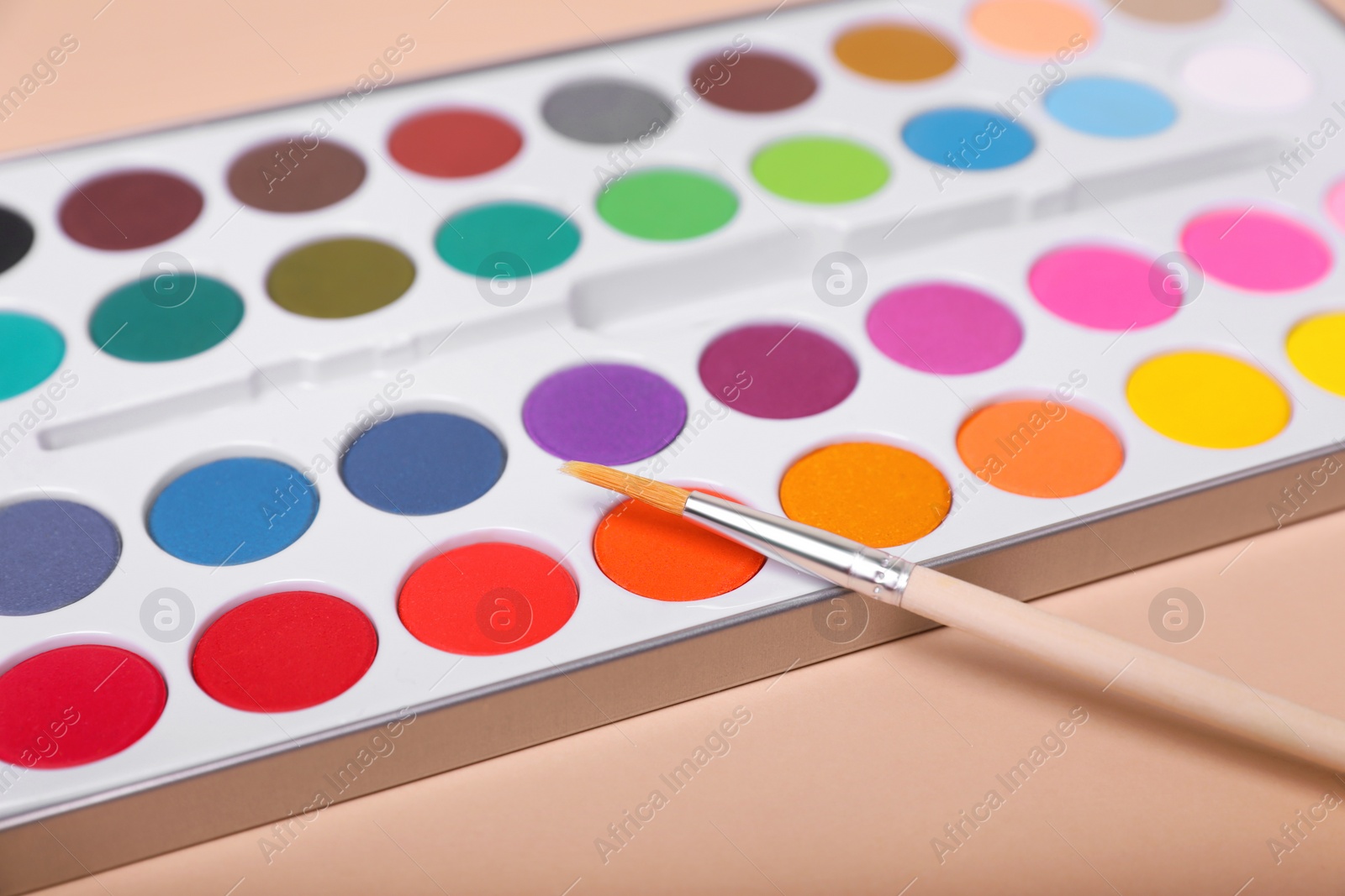 Photo of Watercolor palette with brush on beige background, closeup