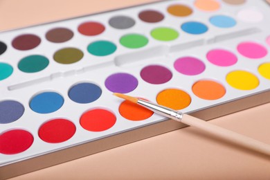 Photo of Watercolor palette with brush on beige background, closeup