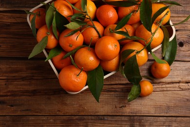 Fresh tangerines with green leaves in crate on wooden table, top view