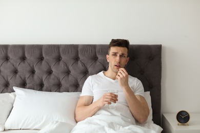 Photo of Young man with terrible headache taking pills in bed