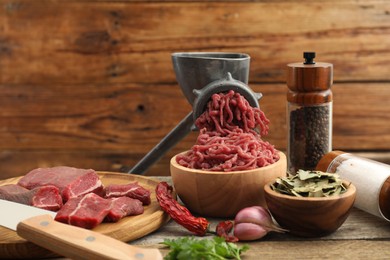 Photo of Manual meat grinder with beef, parsley and spices on wooden table