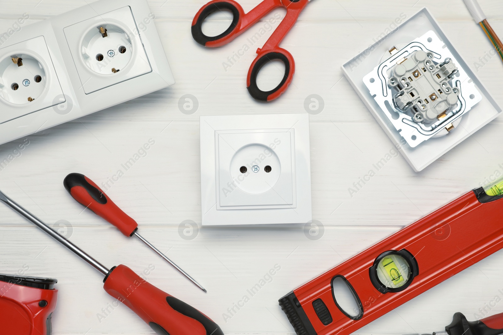 Photo of Power sockets and set of electrician's tools on white wooden table, flat lay