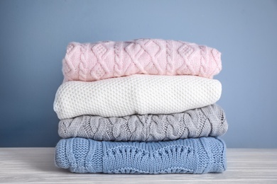 Photo of Stack of folded knitted sweaters on white wooden table against grey background