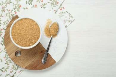 Photo of Brown sugar in bowl and spoon on white wooden table, top view. Space for text