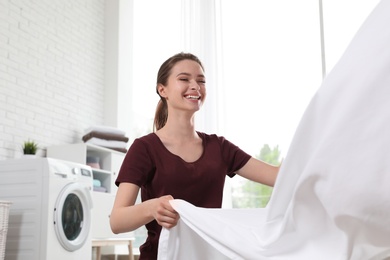 Photo of Young woman with clean bedsheet indoors. Laundry day