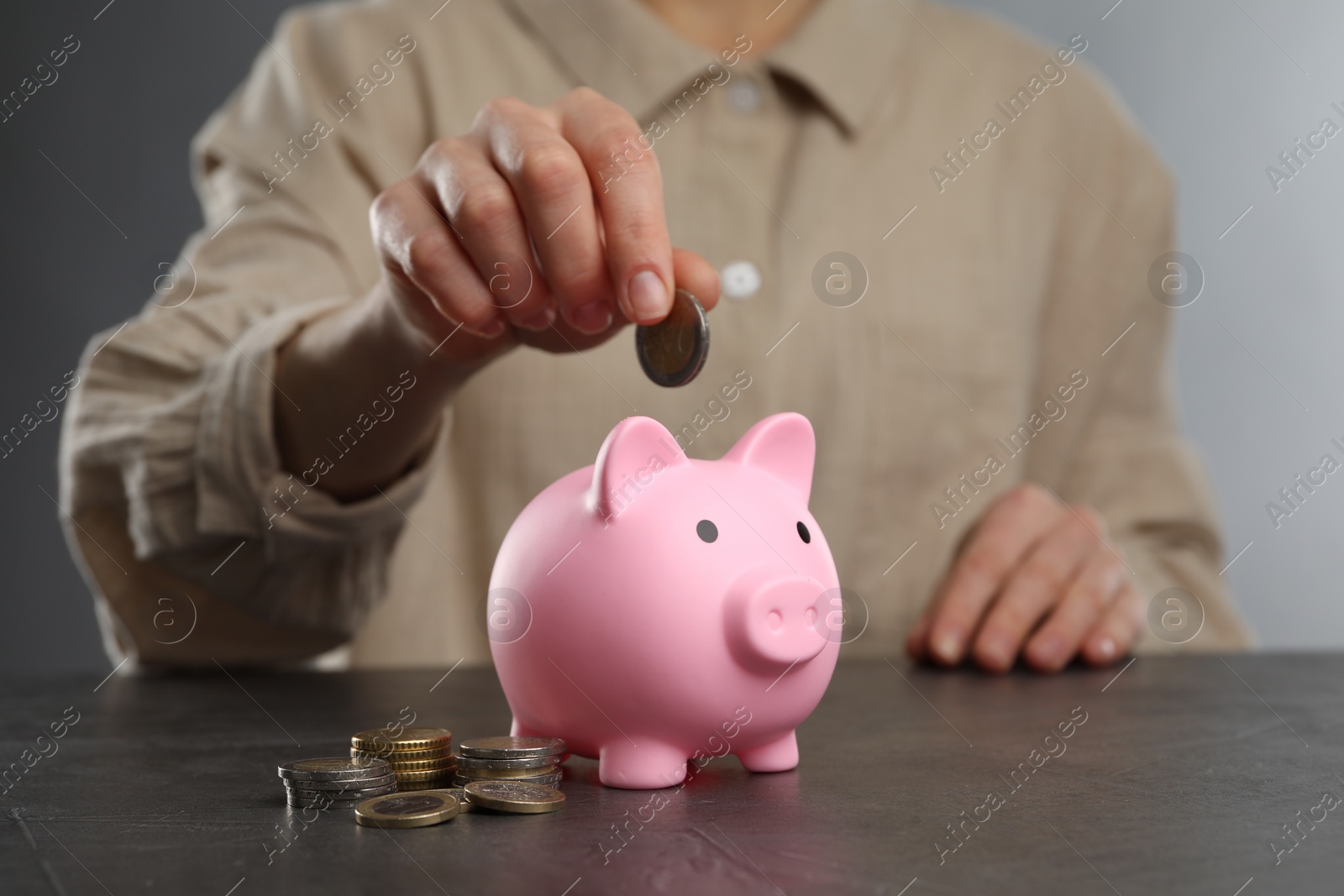 Photo of Woman putting coin into pink piggy bank at black table, closeup