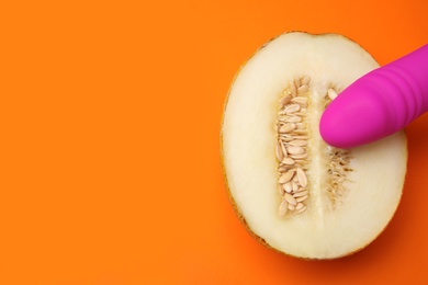 Half of melon and purple vibrator on orange background, flat lay with space for text. Sex concept