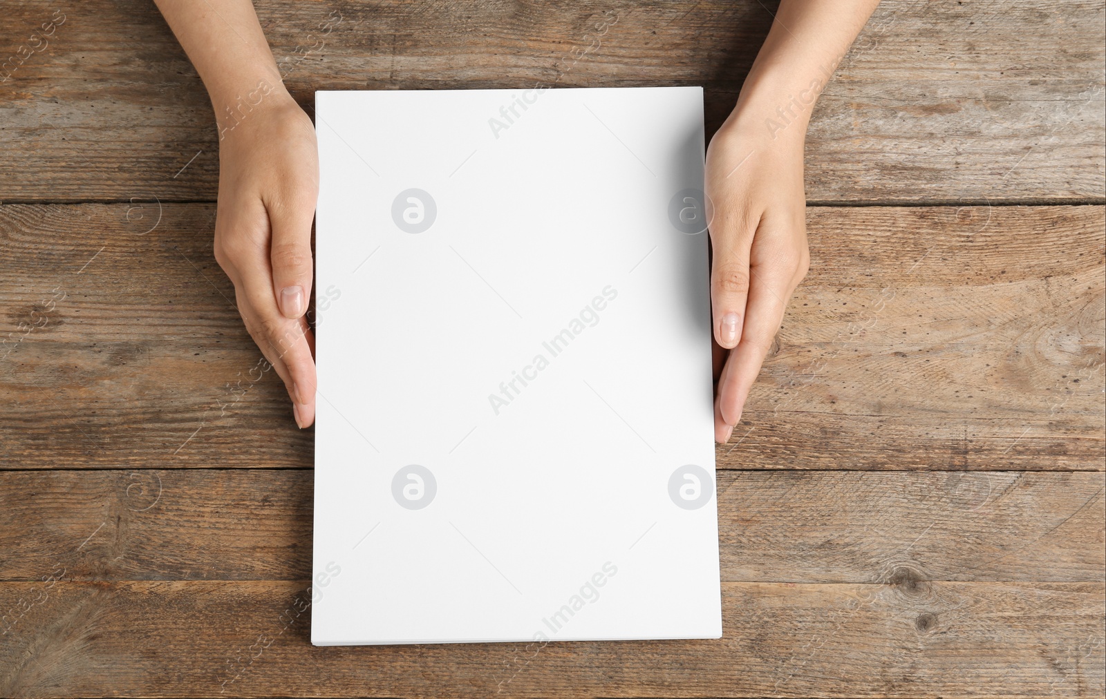 Photo of Woman holding blank paper sheets for brochure at wooden table, top view. Mock up