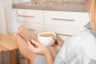 Woman having delicious wafer and coffee for breakfast indoors, closeup