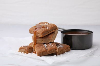 Yummy caramel candies, sauce and sea salt on white table, closeup