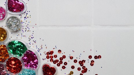 Photo of Many different colorful sequins in containers on white tiled background, flat lay. Space for text