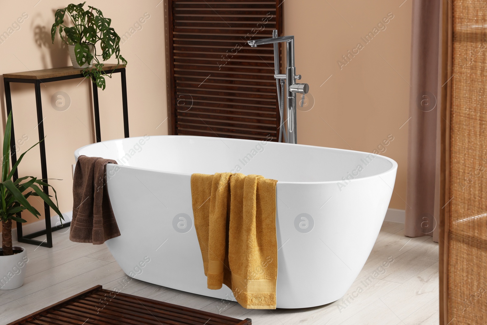 Photo of Stylish bathroom interior with ceramic tub, terry towels and houseplants